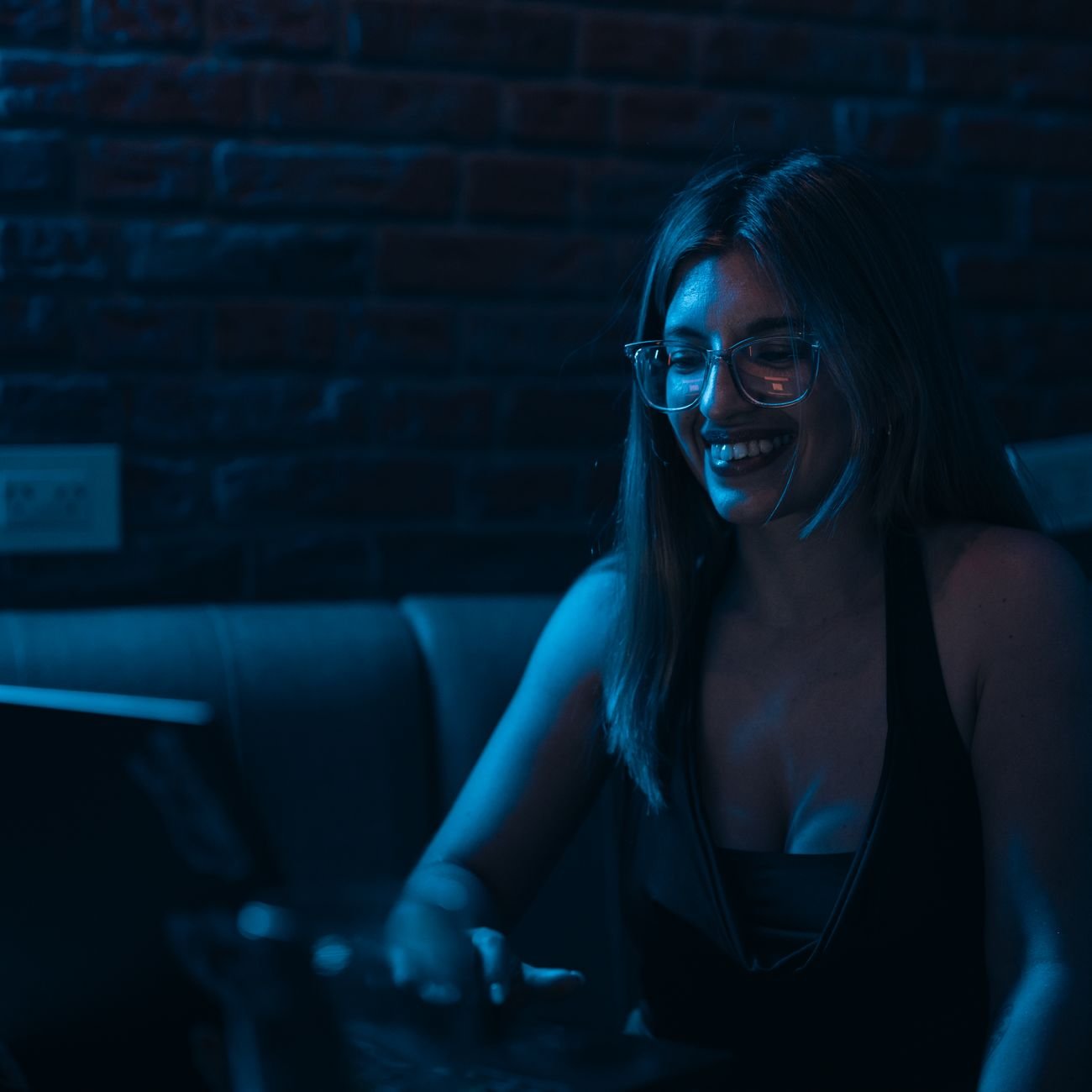 A young woman wearing glasses smiles while working on her laptop.